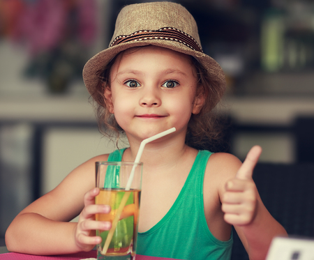 57057824 - happy kid girl drinking apple juice in restaurant and showing thumb up sign